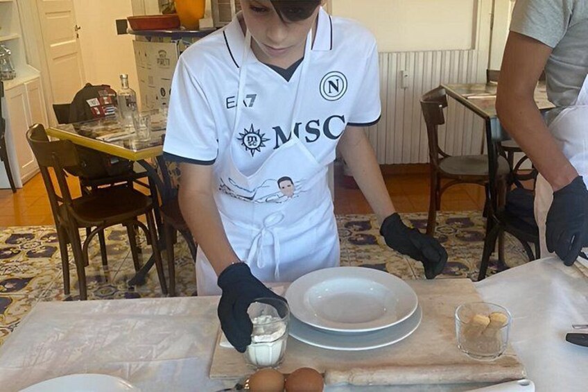 A person in a white apron with a logo, preparing food at a table with a bowl and a glass. 4