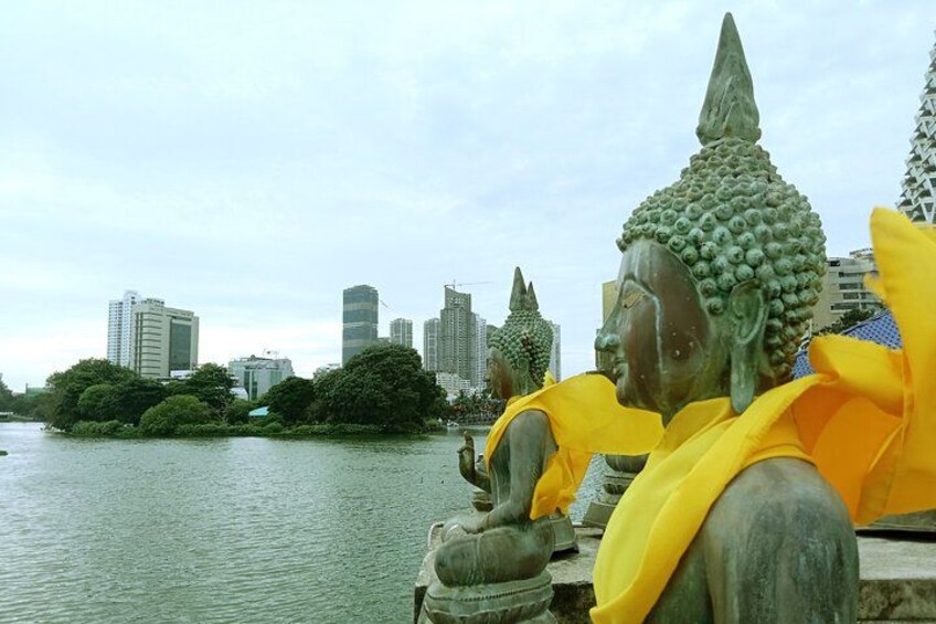 A Buddha statue with a yellow scarf, set against a city skyline and a body of water. 5