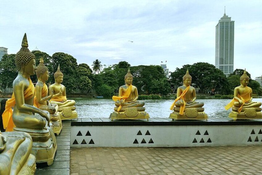 Golden Buddha statues seated by a body of water with a modern building in the background. 4