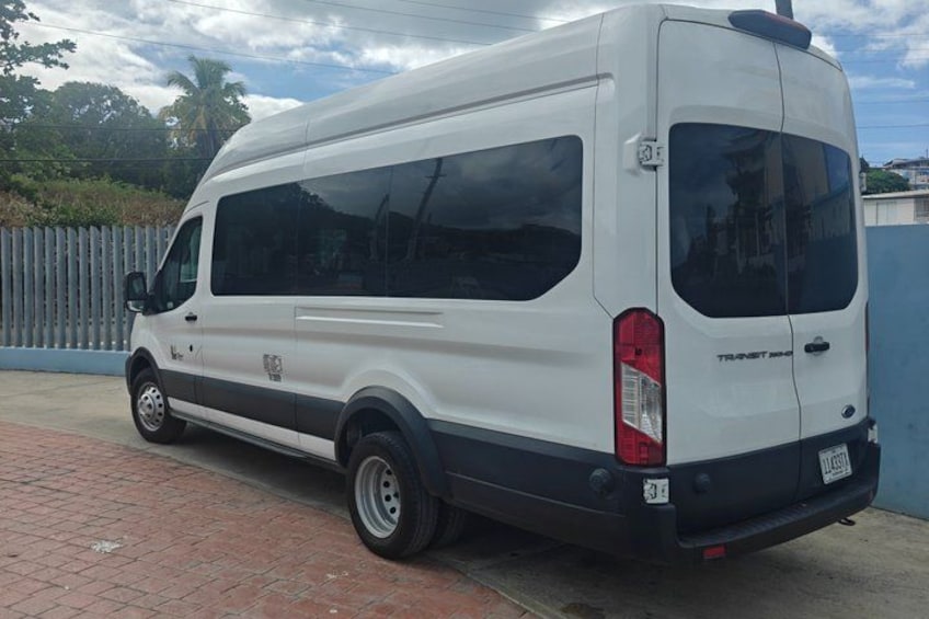 Una camioneta blanca estacionada sobre un pavimento de ladrillo, con una pared azul y una valla al fondo. 2