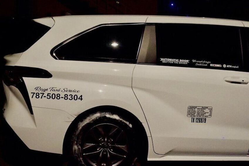 Un coche blanco con un adhesivo lateral que dice 'Rays Taxi Service' y un número de teléfono. 1