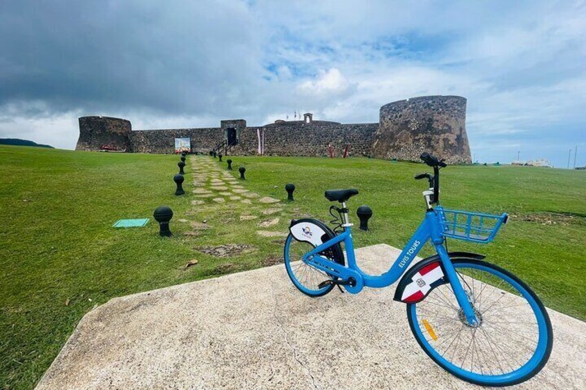 A blue bicycle parked on a concrete path with a historic fort in the background. 2