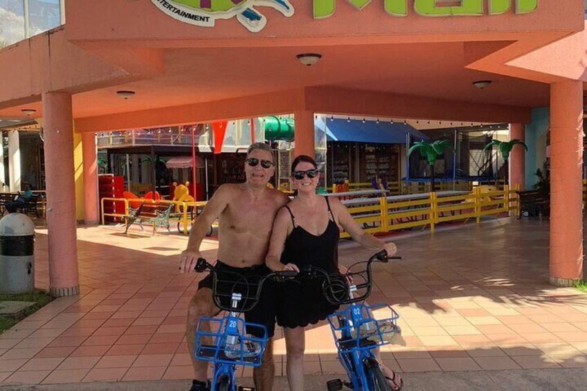 Two people on a bicycle with a basket, in front of a building with a sign that reads "ENTERTAINMENT". 1