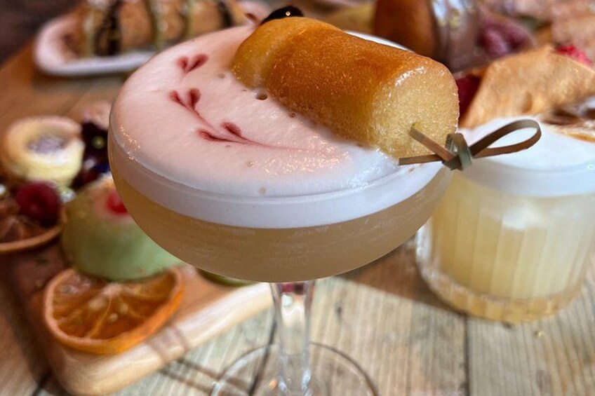 A dessert in a glass with a piece of cake on top, surrounded by various other desserts. 1