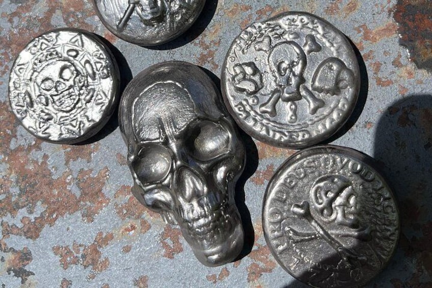 Cinco monedas metálicas con diversos diseños grabados, incluyendo calaveras y figuras, sobre una superficie metálica oxidada. 2