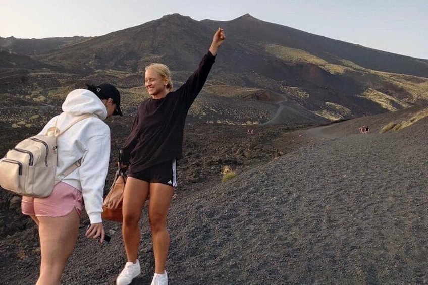 Two people hiking on a volcanic terrain with a mountain in the background. 5