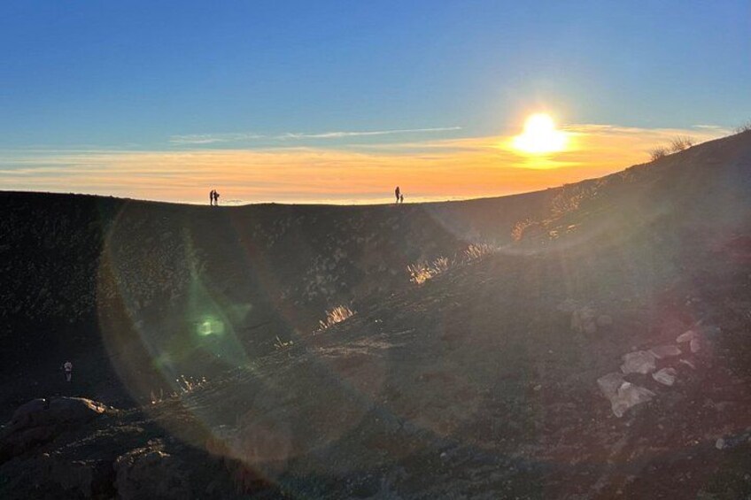 A sunset over a rocky landscape with two people standing on a hill. 2