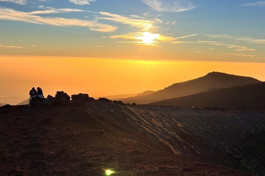 A sunset over a mountainous landscape with a group of people sitting on a rocky outcrop. 3