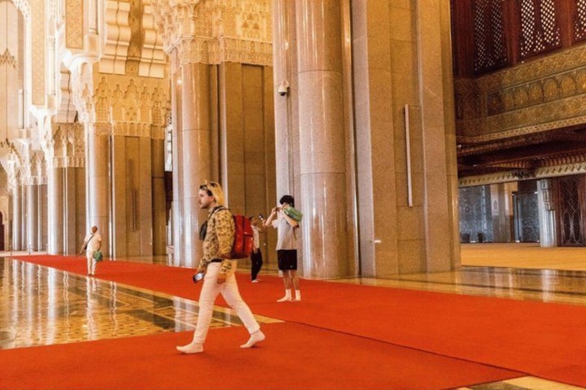 Un intérieur somptueux, avec de hauts plafonds, des colonnes richement décorées et un tapis rouge qui longe le couloir. 2