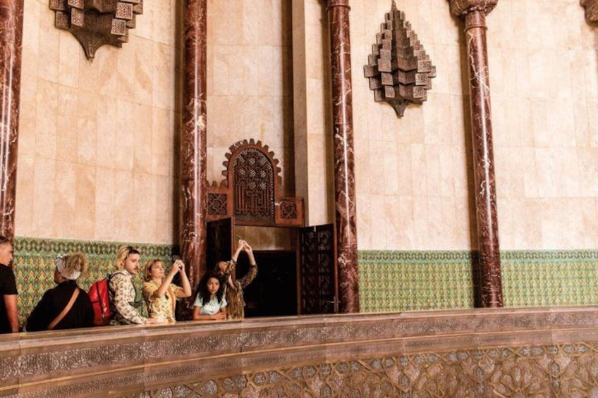 Un groupe de personnes prenant des photos devant un bâtiment orné de colonnes et doté d’une entrée décorative. 1