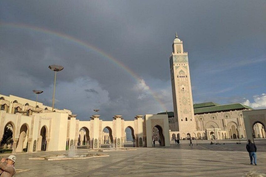 Ein großer, offener Platz mit einem hohen Turm, Bögen und einem Regenbogen. 3