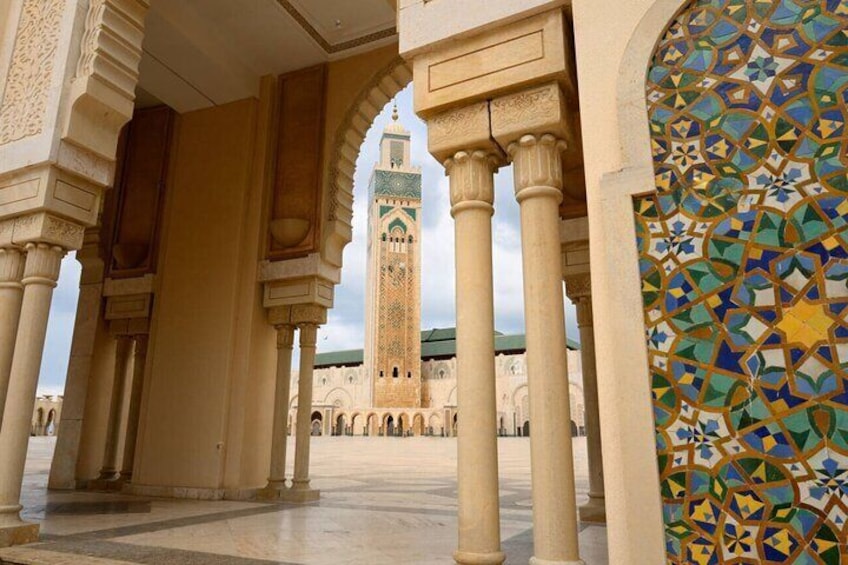 An architectural corridor with arches and columns, leading to a distant tower with a green roof. 1