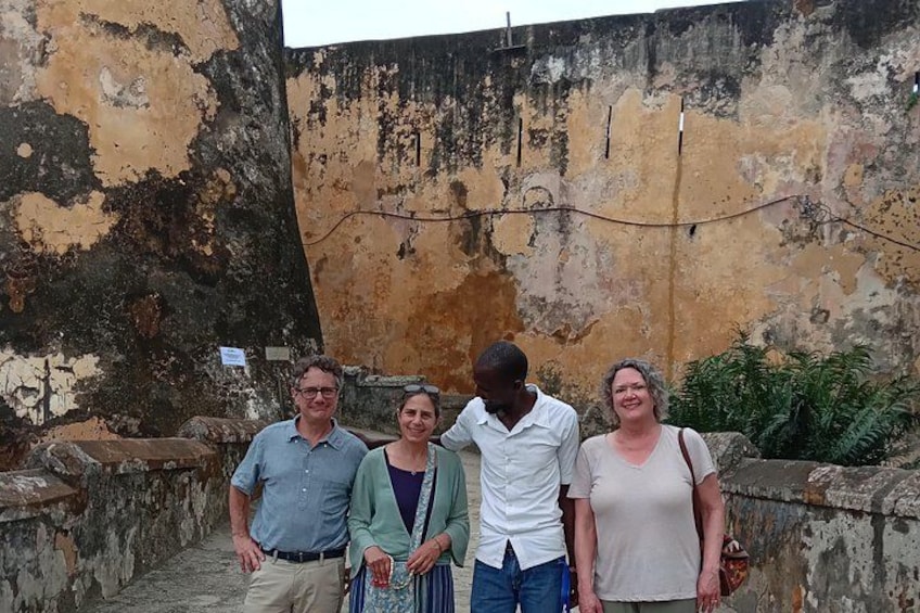 A group of people standing in front of a weathered wall with peeling paint and a small sign. 2