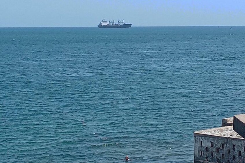Un barco grande en el océano, una persona nadando en el agua y un edificio en la orilla. 2