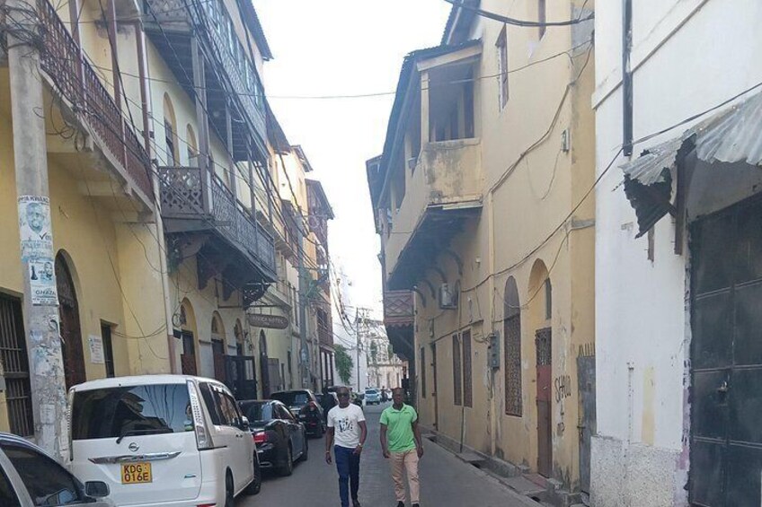 Una calle estrecha bordeada de edificios de varios pisos, coches aparcados y peatones. 4