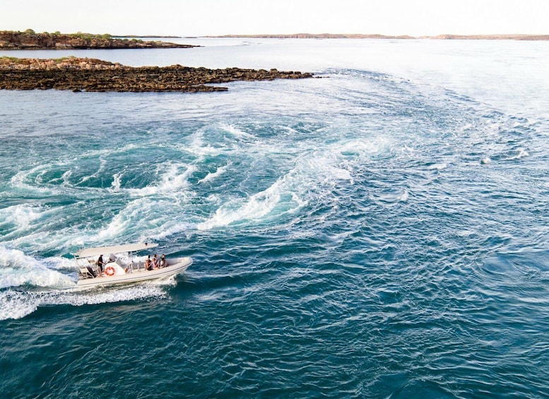 A boat moving through choppy waters with a rocky shoreline in the background. 1
