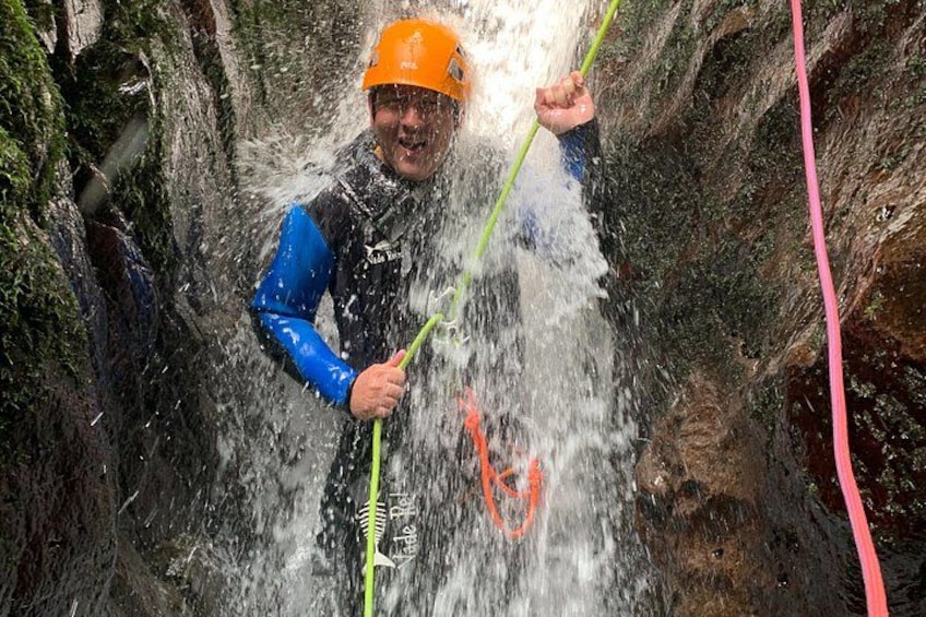 A person in a blue wetsuit and orange helmet holding a green pole, standing in a water-filled crevice with a red rope. 4