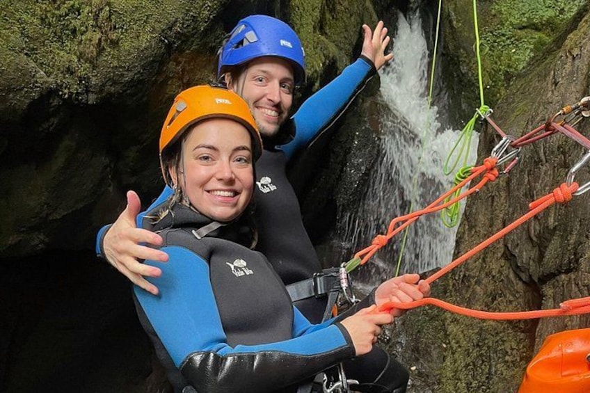 Two people rappelling down a rocky cliff with a waterfall in the background. 2