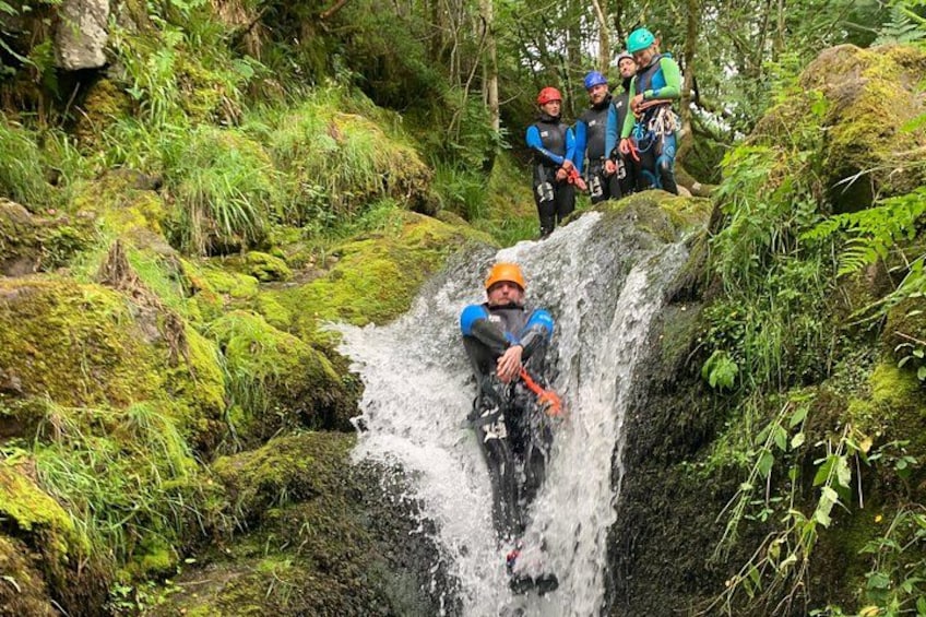 A person in blue wetsuit and orange helmet navigating a waterfall in a forested area. 3