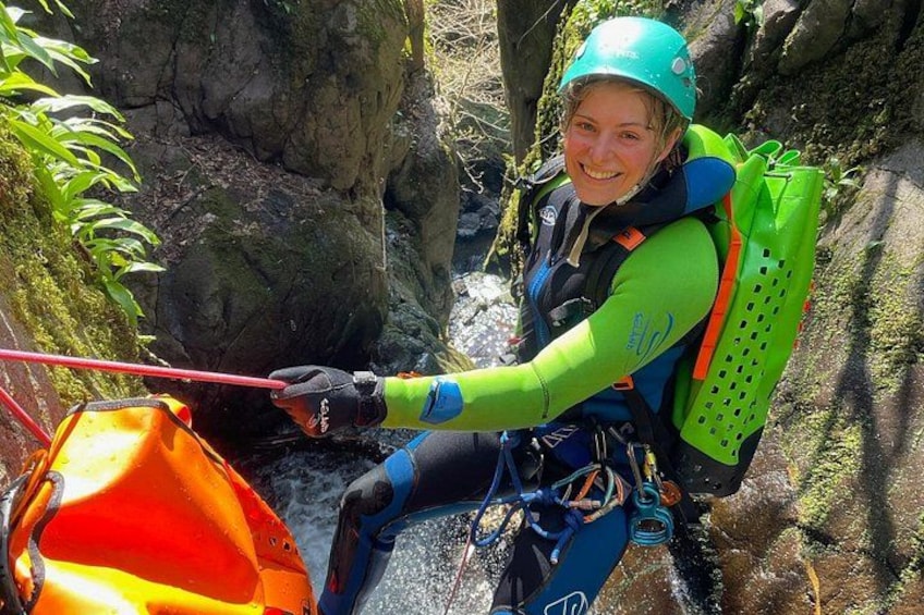 A person rappelling down a rocky cliff with a green helmet and a backpack. 1