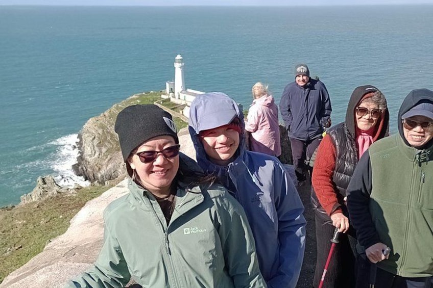 Un grupo de personas de pie en un acantilado con vistas al mar, con un faro al fondo. 2