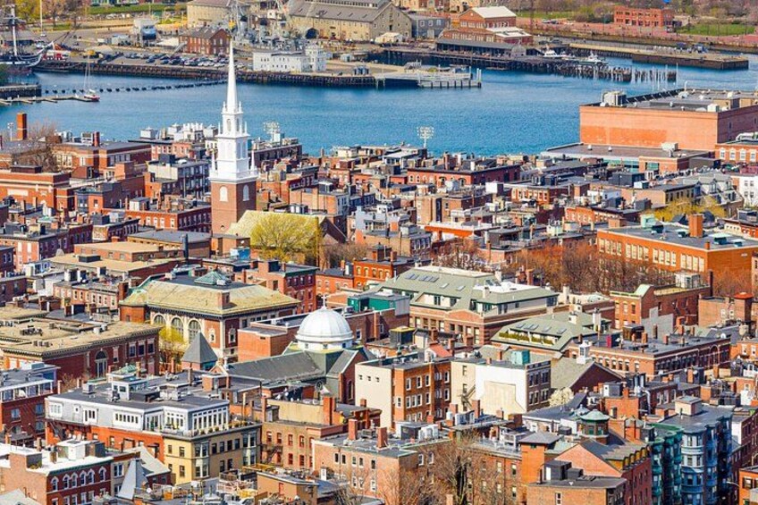 A densely packed urban area with historic buildings, a prominent church steeple, and a waterfront. 5