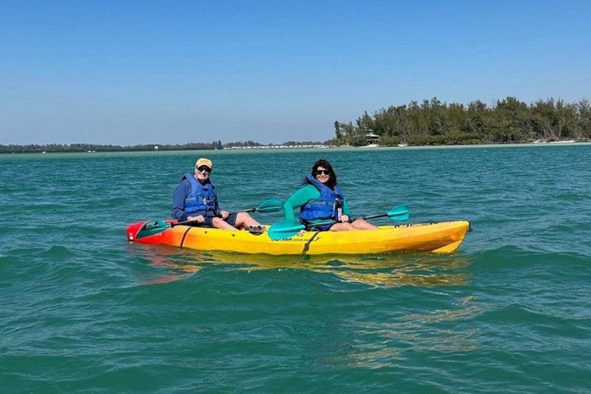Two people kayaking on calm water with a clear sky and a distant shoreline. 5