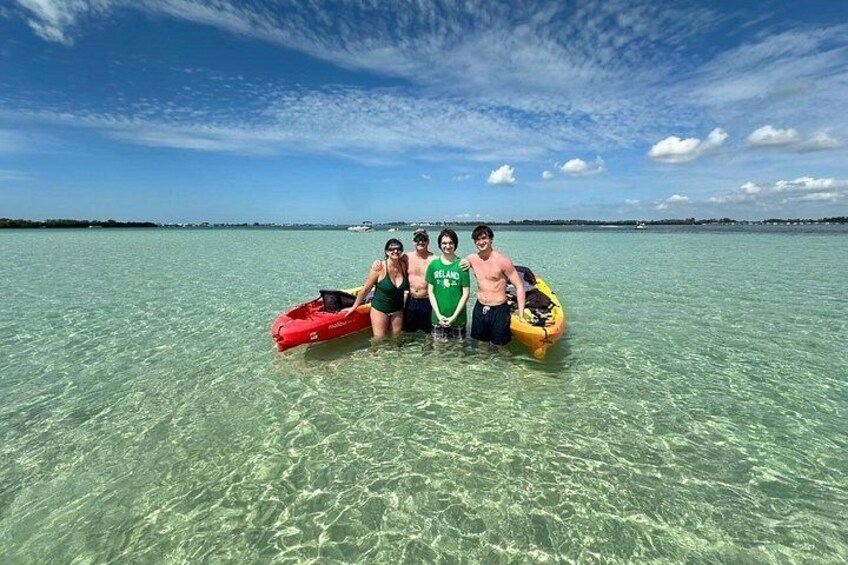 Four people in a shallow, clear body of water with a boat and a kayak. 3