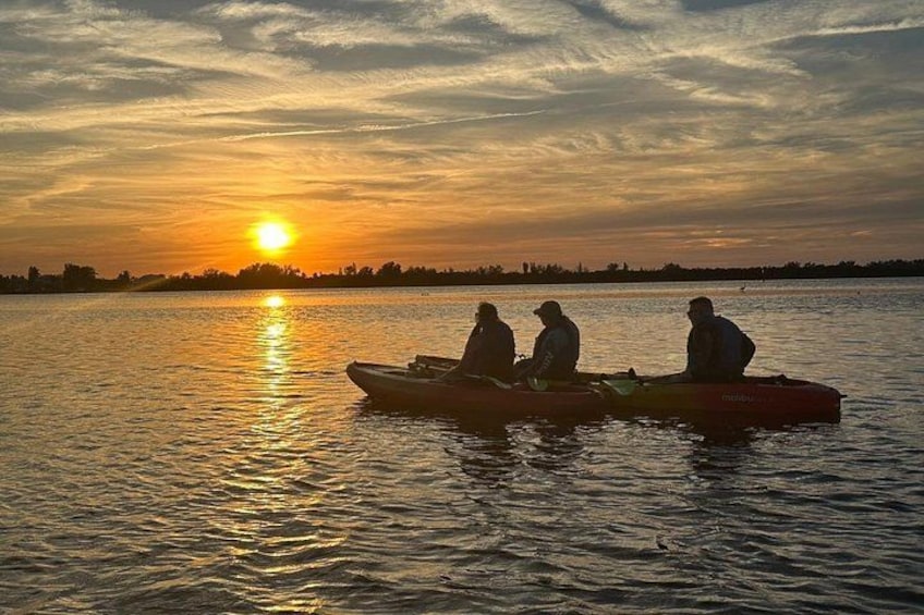 Three people in kayaks on a calm body of water during sunset. 5
