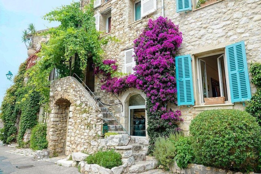 A stone building with a staircase, a door, and a window with blue shutters. 1