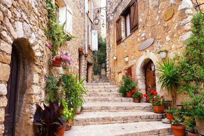 A narrow stone staircase leading up to a building with arched doorways, surrounded by potted plants and flowers. 2
