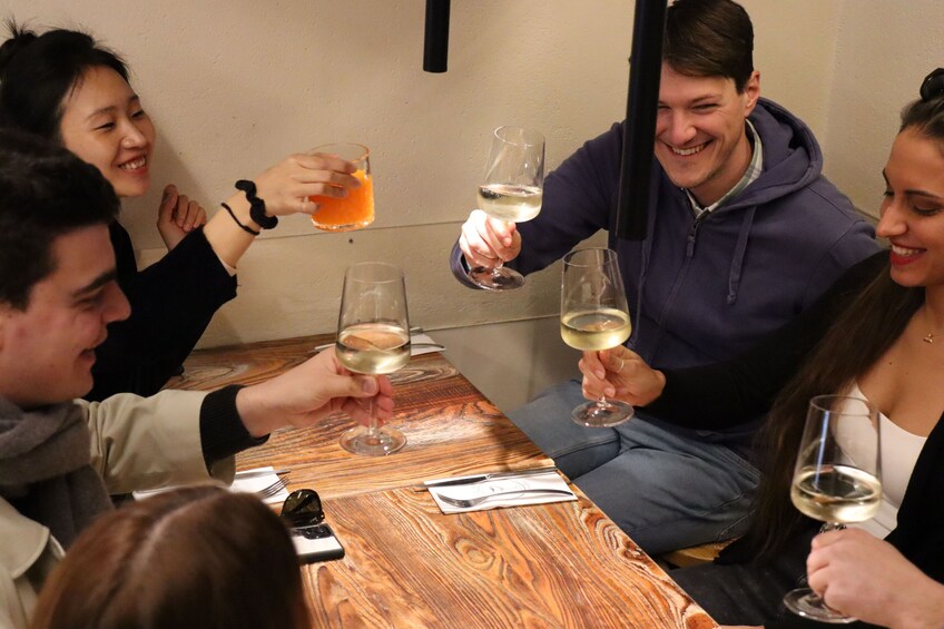 A group of people toasting with glasses of white wine at a wooden table. 5