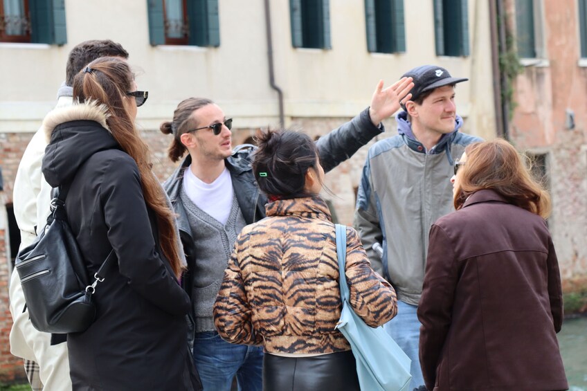 A group of people standing outdoors, some wearing jackets, in front of a building with windows. 2