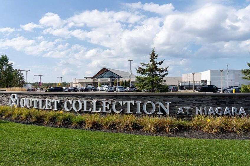 A sign for Outlet Collection at Niagara with a parking lot and buildings in the background. 3