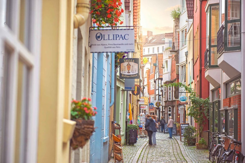 A cobblestone street lined with colorful buildings, a sign for 'Lillipac' and 'Grogg Antiquitaten', and bicycles parked on the right. 5