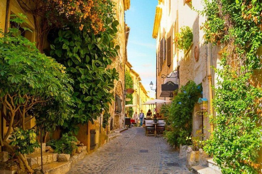 A cobblestone street lined with buildings, some with vines, and a few people in the distance. 2