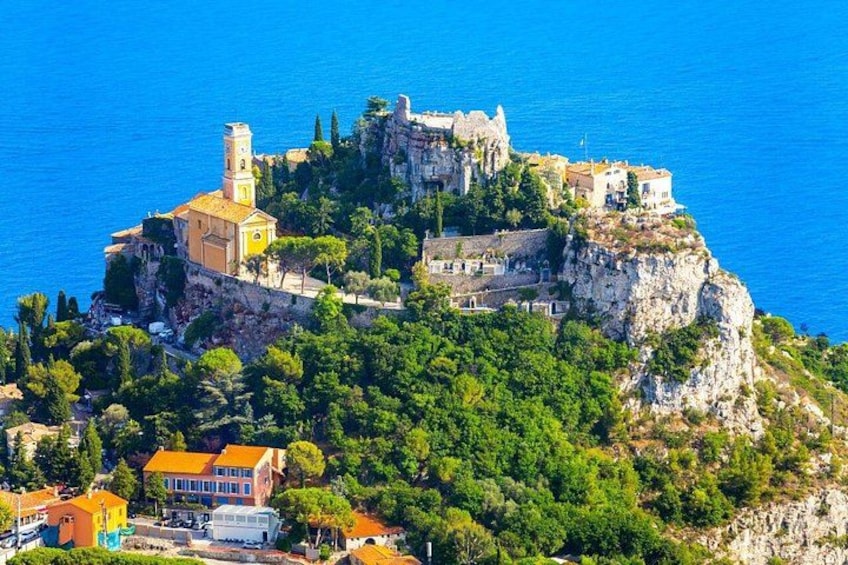 A coastal town with a prominent castle on a cliff, lush greenery, and a clear blue sea. 4