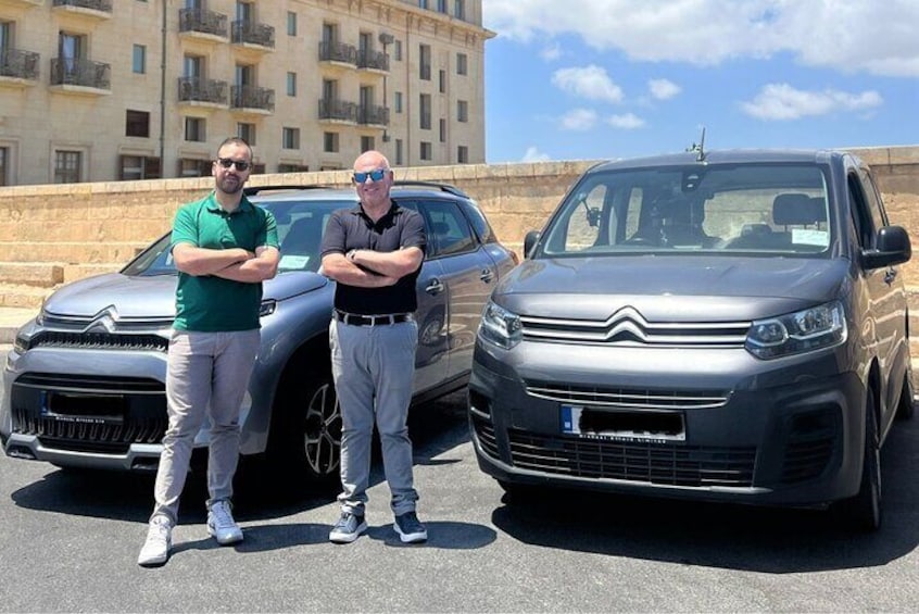 Two men standing in front of two cars parked on a street. 4