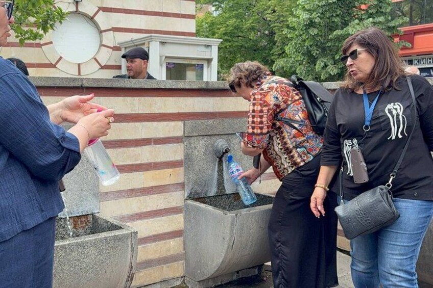 People near a fountain with a patterned wall and a circular design in the background. 2