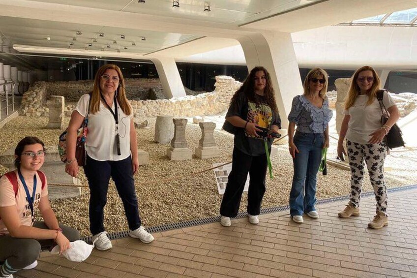 A group of people in an outdoor museum setting with stone structures and a modern architectural roof. 4
