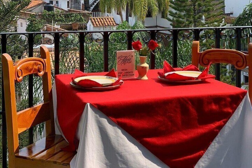 A dining table with a red tablecloth, two chairs, a vase with flowers, and a menu on a balcony. 5