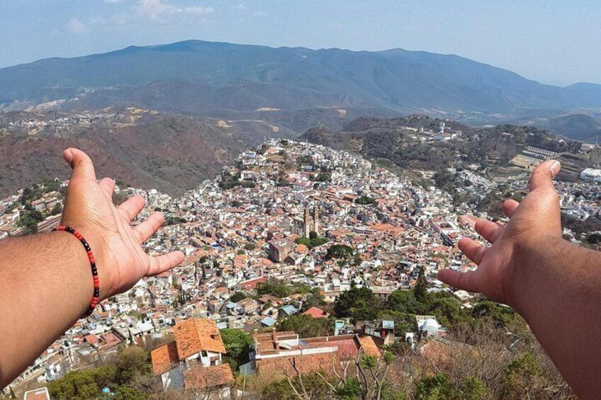 A hand reaching out towards a town nestled in a valley with mountains in the background. 3