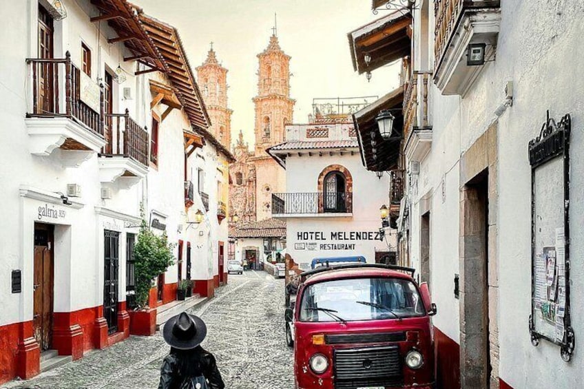 Una calle adoquinada con un coche rojo estacionado frente a un edificio con la leyenda 'Hotel Melendez'. 1
