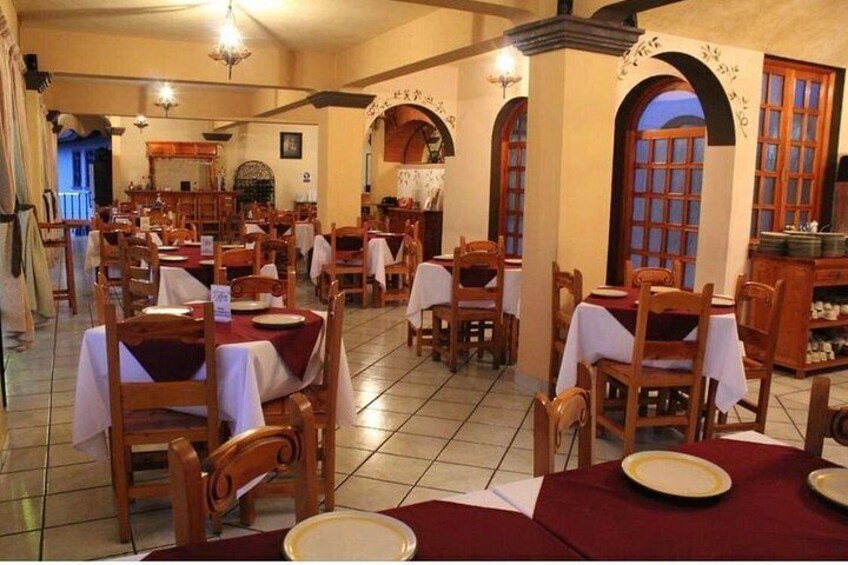 A restaurant with wooden tables and chairs, arched windows, and tiled floors. 4