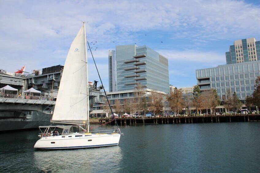 A sailboat on a calm river with modern buildings in the background. 2