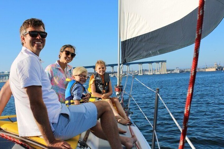 A family on a sailboat with a bridge in the background. 1