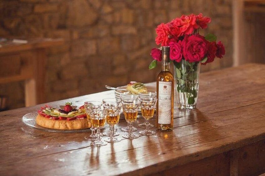 A wooden table with a dessert, glasses, a bottle, and a vase of flowers. 5