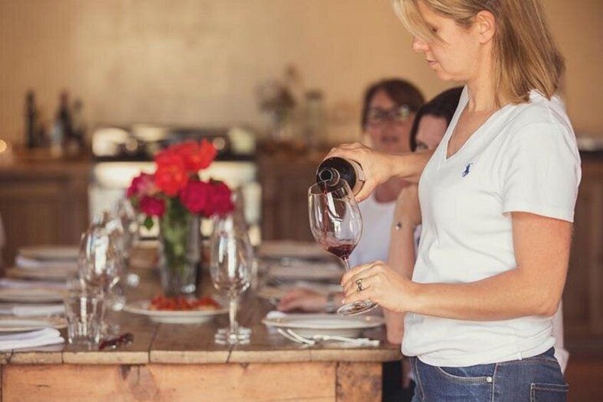 A person pouring wine into a glass at a dining table with a vase of flowers. 1