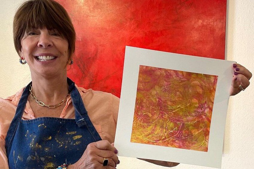 A person holding a framed abstract painting with visible paint splatters. 2