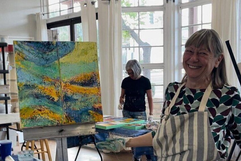 An artist painting a colorful abstract piece on a canvas in a well-lit room with large windows. 1